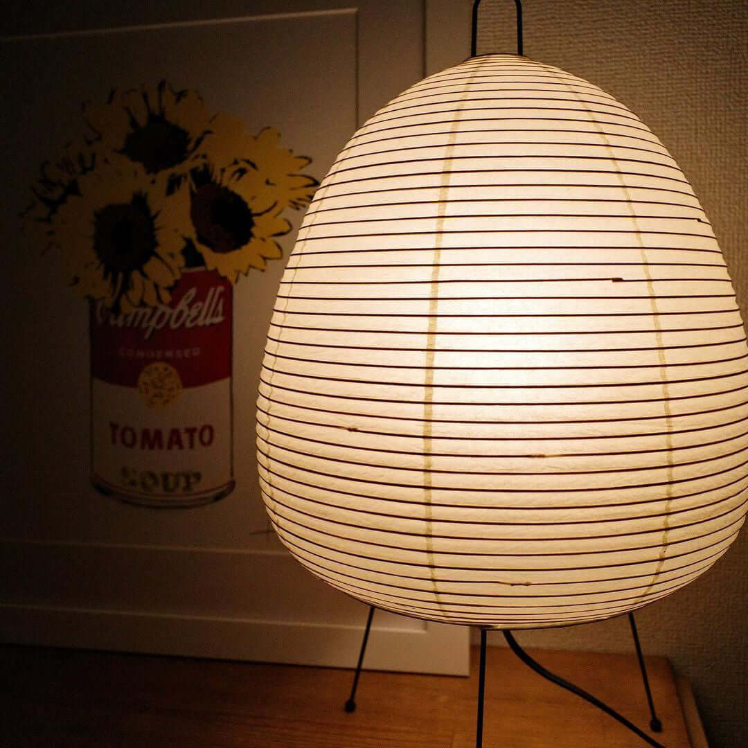 Close view of the ribbed paper shade on this Clérachic table lamp, glowing in front of a pop-art style poster.