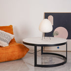 Egg-shaped Clérachic lamp on a round marble-topped coffee table, with an orange lounge chair and framed art behind.