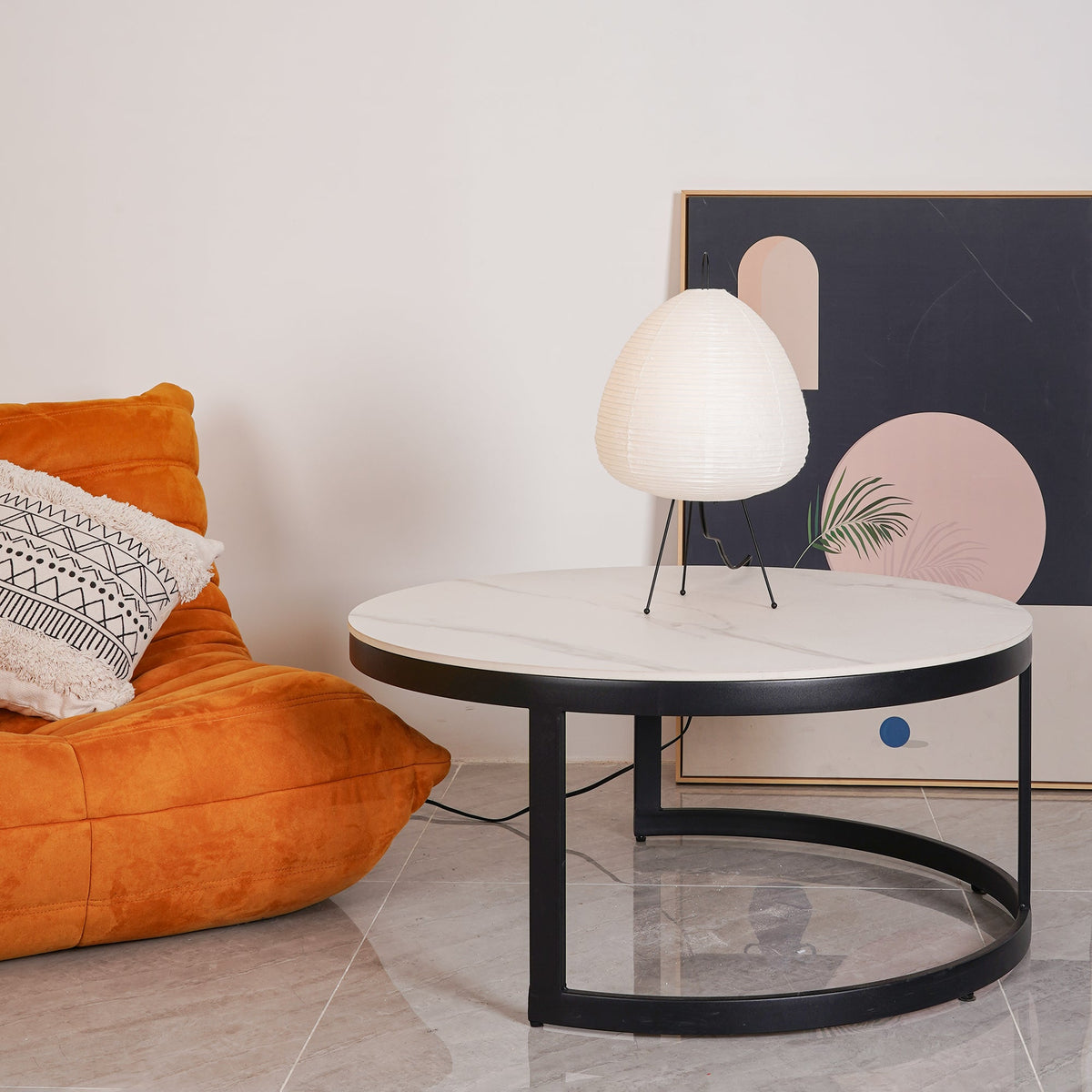 Egg-shaped Clérachic lamp on a round marble-topped coffee table, with an orange lounge chair and framed art behind.