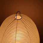 Close view of the ribbed paper shade and black wire hanging loop on this Clérachic lamp, glowing amber.
