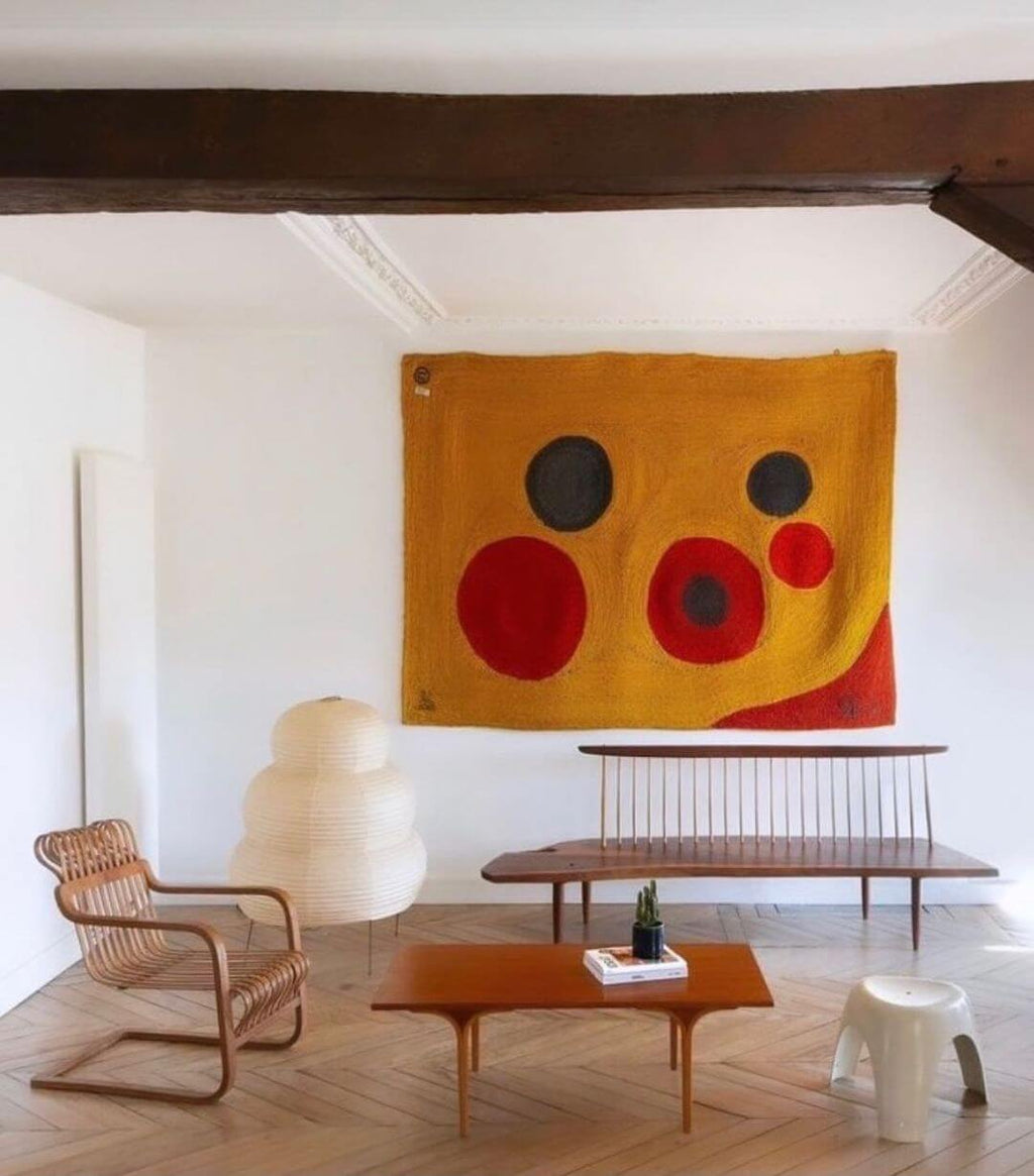 This Clérachic tiered paper lamp sits in a white room with a wooden beam, a bold wall hanging and a low coffee table.