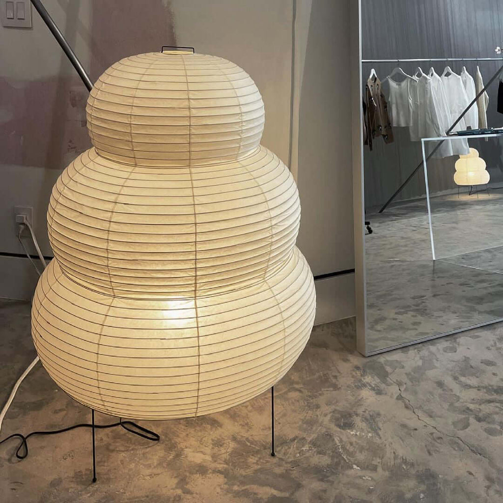 A very large tiered Clérachic paper lamp on a concrete-look floor, with a clothes rail reflected in the mirror behind.