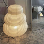 A very large tiered Clérachic paper lamp on a concrete-look floor, with a clothes rail reflected in the mirror behind.