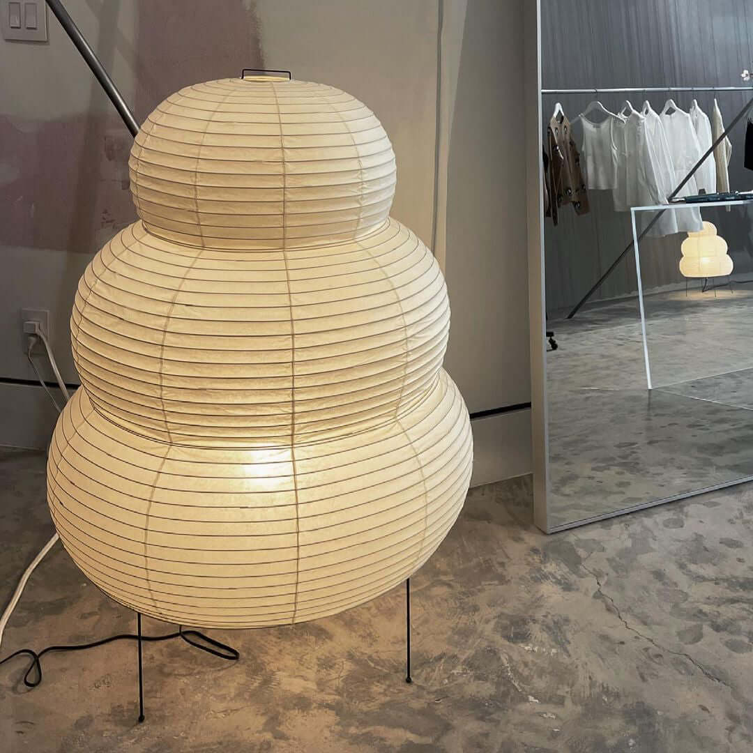 A very large tiered Clérachic paper lamp on a concrete-look floor, with a clothes rail reflected in the mirror behind.