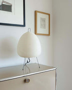 Egg-shaped Clérachic paper lamp on a steel sideboard, with a framed drawing on the pale wall above.