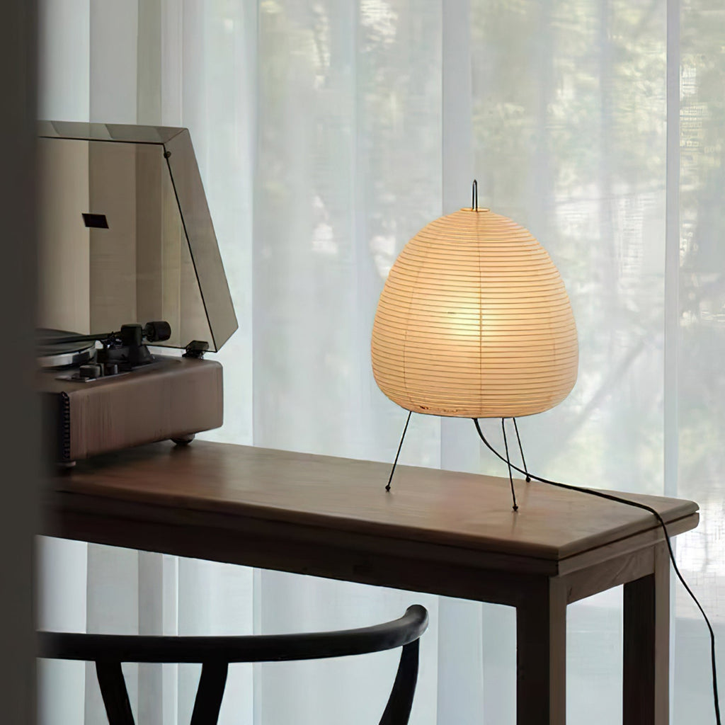 This Clérachic paper lamp lit on a dark wooden desk beside a record player, with sheer curtains behind and a black cord at the edge.