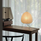 This Clérachic paper lamp lit on a dark wooden desk beside a record player, with sheer curtains behind and a black cord at the edge.