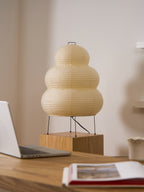 Clérachic tiered paper lamp on a wooden block, seen from a distance with a laptop and an open book on the desk.