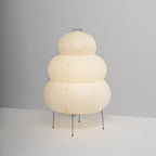 This Clérachic tiered paper lamp stands on four black legs against a plain grey backdrop, shown from the front.