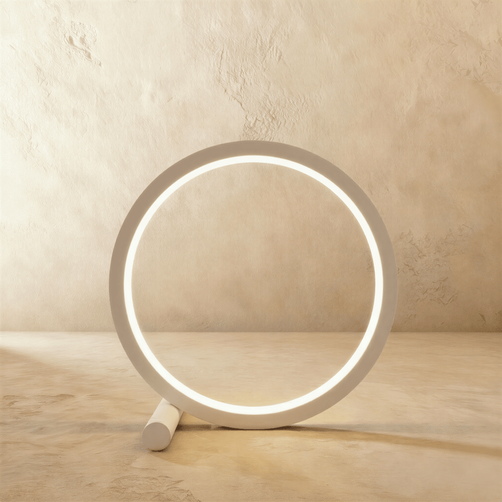 Clérachic white ring-shaped touch lamp glowing warm on its short cylindrical foot, set against a limewash wall.
