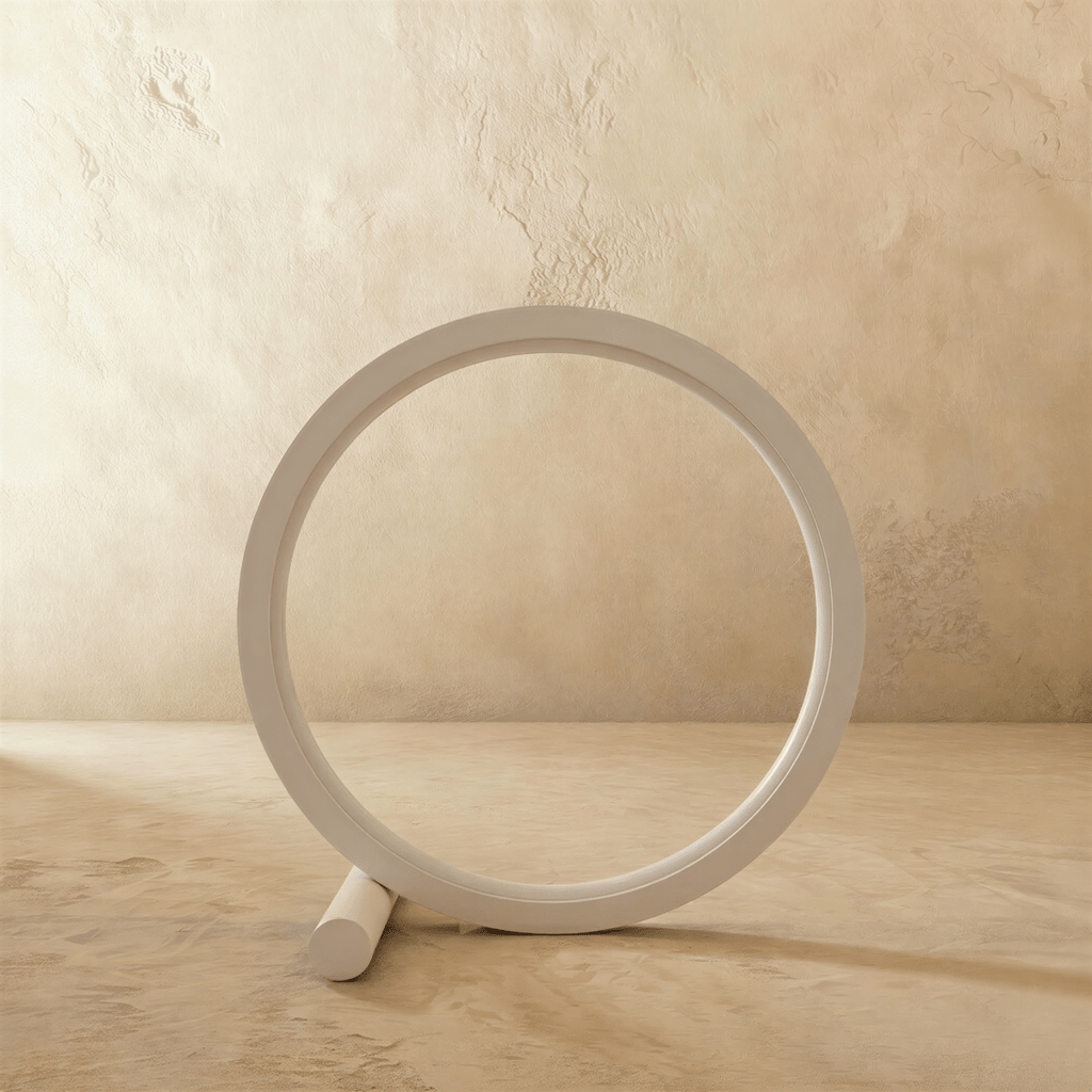 Clérachic white ring table lamp switched off, a slim aluminium circle resting on a small round foot in front of a plaster wall.