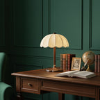 This Clérachic table lamp stands on a dark wooden desk beside an open book, a globe and framed photographs, against a deep green wall.