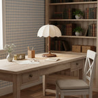 Scalloped Clérachic table lamp on a pale wooden writing desk, in front of a bookcase and a blue gingham wall panel.