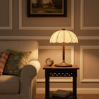 Warm glow from this Clérachic table lamp on a carved dark side table beside an armchair with a floral cushion.