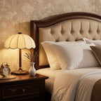 A Clérachic table lamp lights a dark wood nightstand beside a buttoned headboard, with an alarm clock and a vase of lavender.
