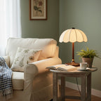 Clérachic table lamp on a round side table beside a cream armchair, with an open book, a cup and a fern.