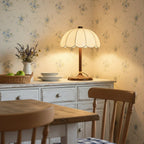 Lit scalloped Clérachic table lamp on a white painted dresser, with a bowl of green apples and a jug of lavender nearby.