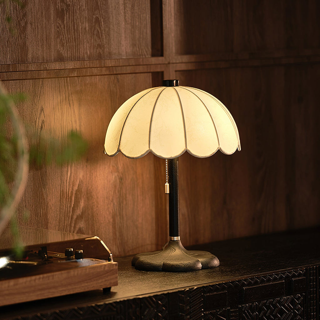 Glowing Clérachic table lamp with a black stem and bronze-toned base, on a dark carved console against a wood-panelled wall.