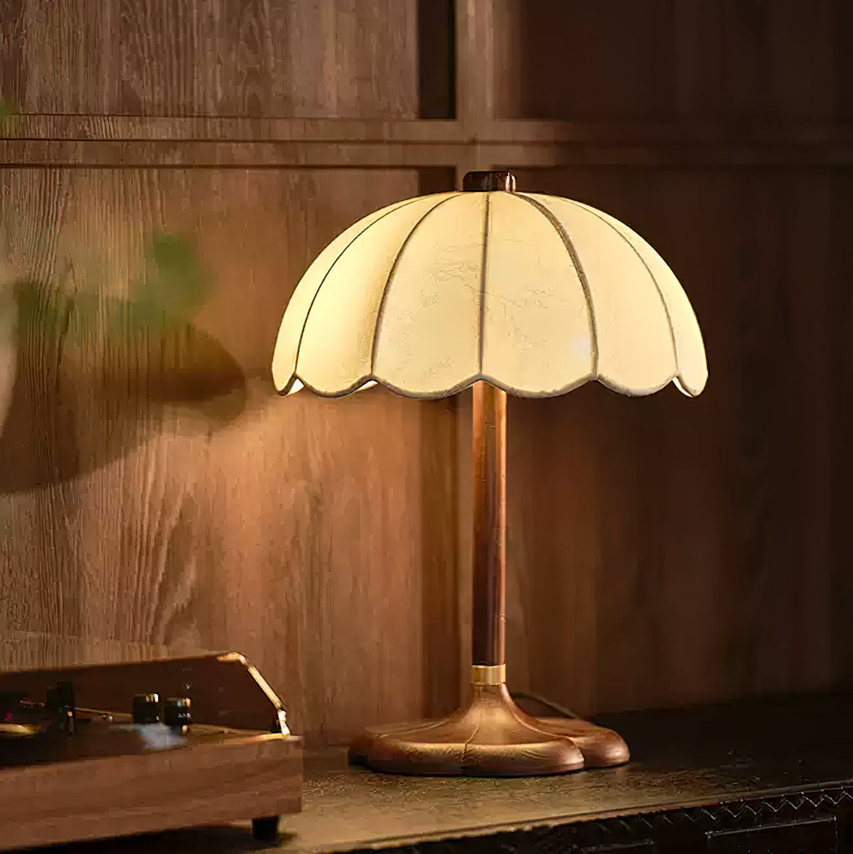 Clérachic table lamp with a walnut-coloured stem on a dark console, lit warm against a wood-panelled wall beside a record player.