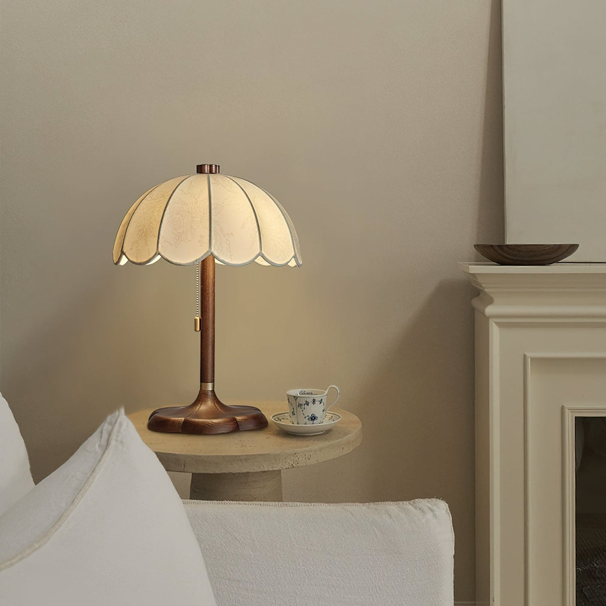 Lit Clérachic table lamp on a low table with a teacup and saucer, beside a white sofa and a white mantel.