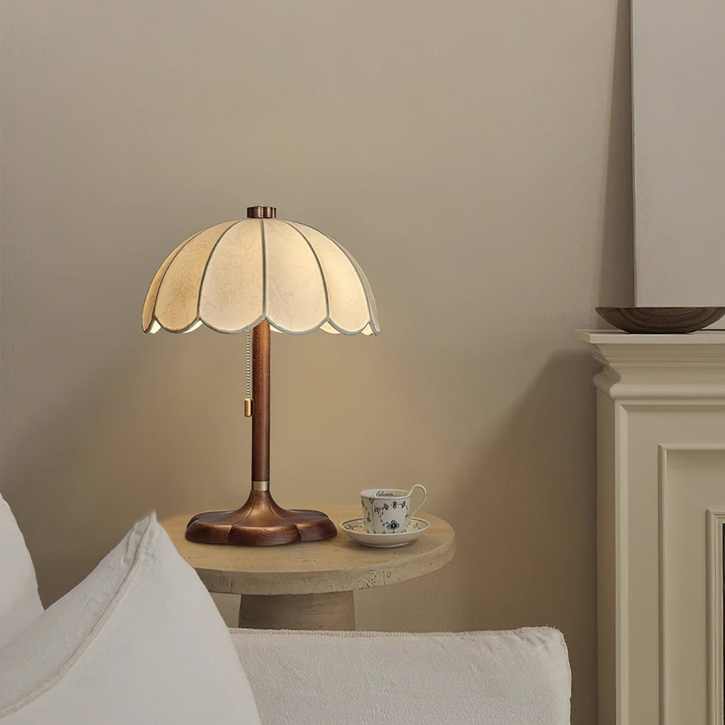 Clérachic table lamp with a scalloped shade beside a small stone table with a patterned teacup, next to a white sofa.