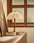 Clérachic table lamp on a wooden cabinet by a window with a patterned glass pane, with a short stack of books at its foot.