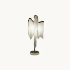 A Clérachic table lamp in silver on a plain white backdrop, its draped chain fringe falling from a curved top to a round base.