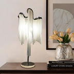 This Clérachic tassel lamp lit on a dark console beside a vase of peach tulips, with a framed abstract print behind it.
