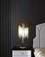 This Clérachic lamp glowing on a white bedside chest with a gold handle, set against a dark panelled wall and a grey headboard.