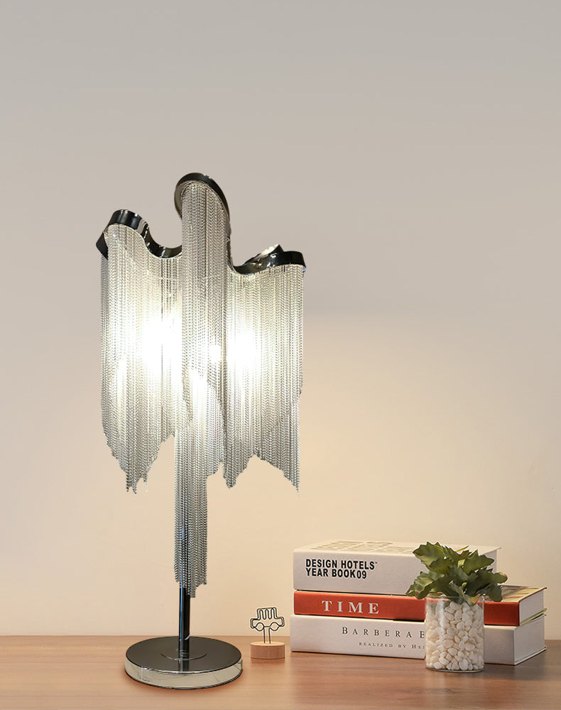 This Clérachic lamp on a wooden desk, beside a few stacked books, a small plant and a tiny figure, against a peach wall.