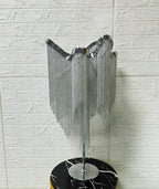 Rear three-quarter view of this Clérachic lamp unlit, its silver chains hanging in curtains over a black marble stool.