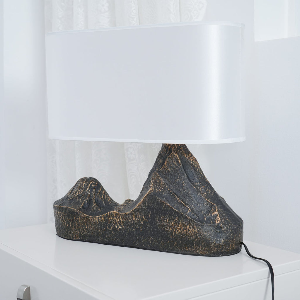 Low side view of this Clérachic table lamp, its broad white shade above a ridged twin-peak base, with a black cord on a white surface.