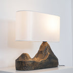 Angled view of the glossy white shade and the rugged twin-peak base of this Clérachic table lamp, on a white cabinet top.