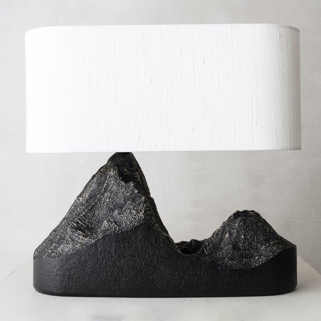 Close view of a wide cream shade over the rough bronze-streaked peaks of this Clérachic table lamp's black base.