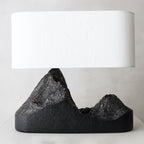 Close view of a wide cream shade over the rough bronze-streaked peaks of this Clérachic table lamp's black base.
