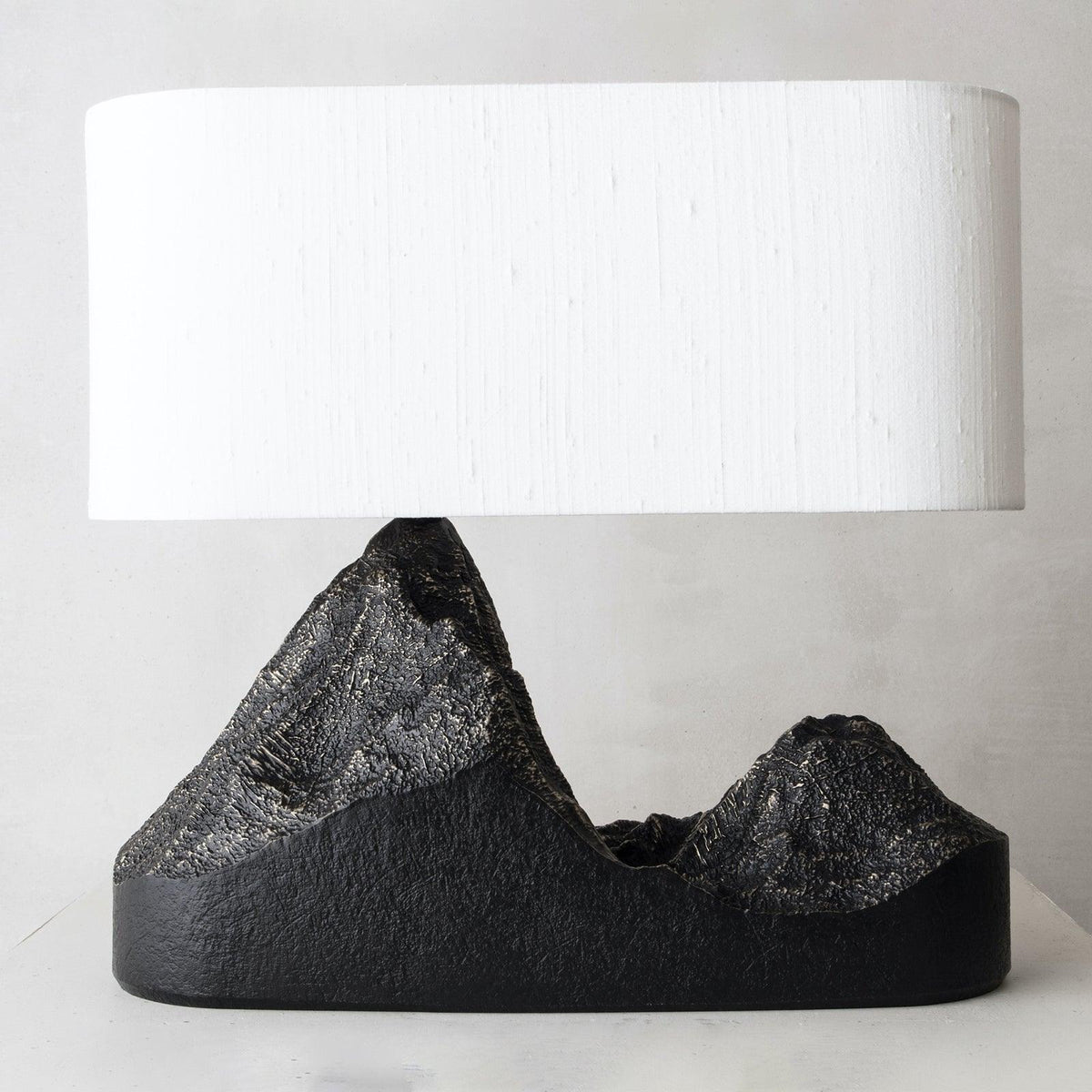 Close view of a wide cream shade over the rough bronze-streaked peaks of this Clérachic table lamp's black base.