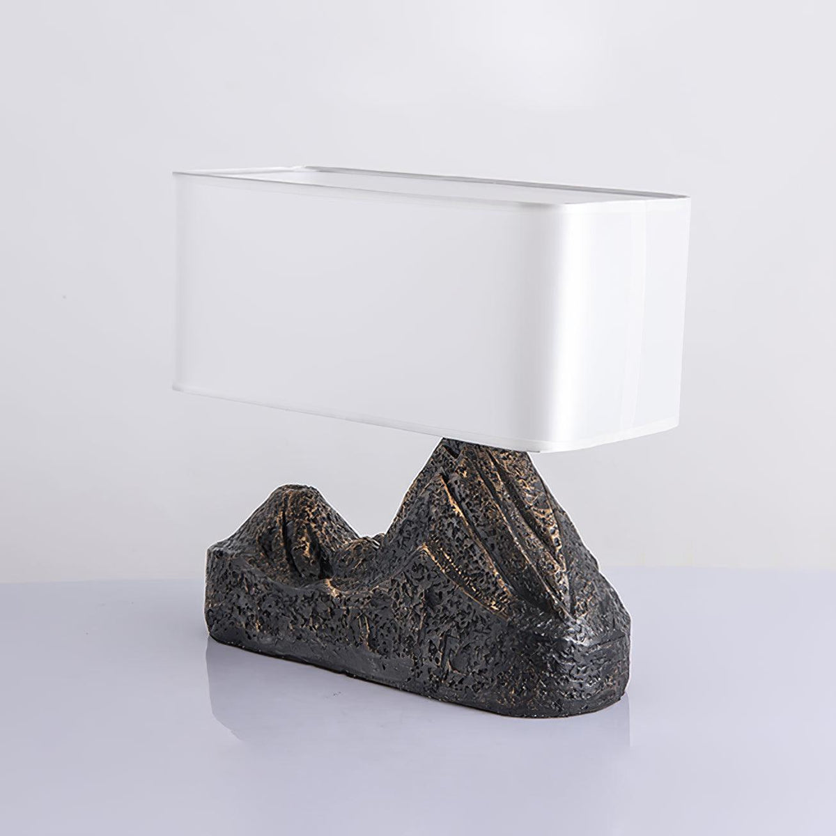 Angled view of a Clérachic table lamp with a glossy white shade and a rugged bronze-brown mountain base, on a pale surface.