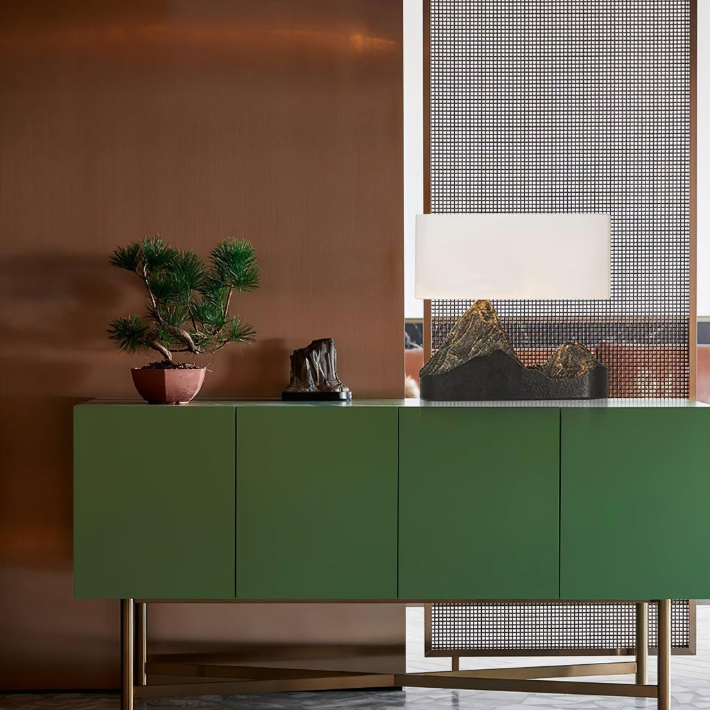 A Clérachic mountain-base table lamp on a green sideboard with brass legs, beside a bonsai and a small sculpture.