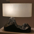 Close view of a lit cream shade above the bronze-flecked peaks of this Clérachic table lamp's dark base.
