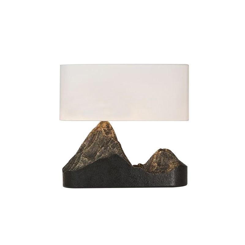 Front view of a Clérachic table lamp, a rectangular white shade over a dark twin-peak base with bronze peaks, on white.