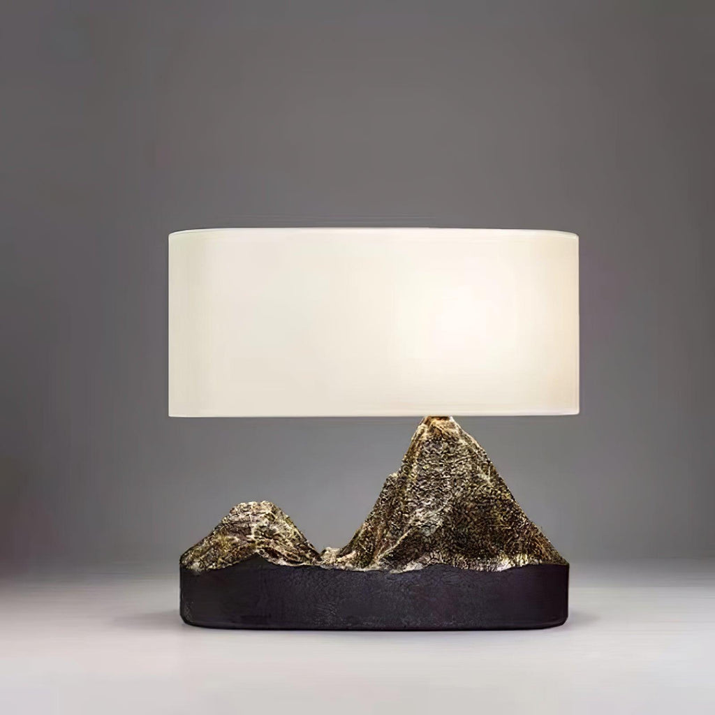 This Clérachic table lamp lit against a dark grey backdrop, its white shade above a black base with glinting bronze peaks.