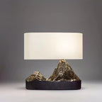 This Clérachic table lamp lit against a dark grey backdrop, its white shade above a black base with glinting bronze peaks.