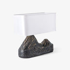 Angled studio view of a Clérachic table lamp with a boxy white shade and a rough bronze-brown mountain base, on light grey.