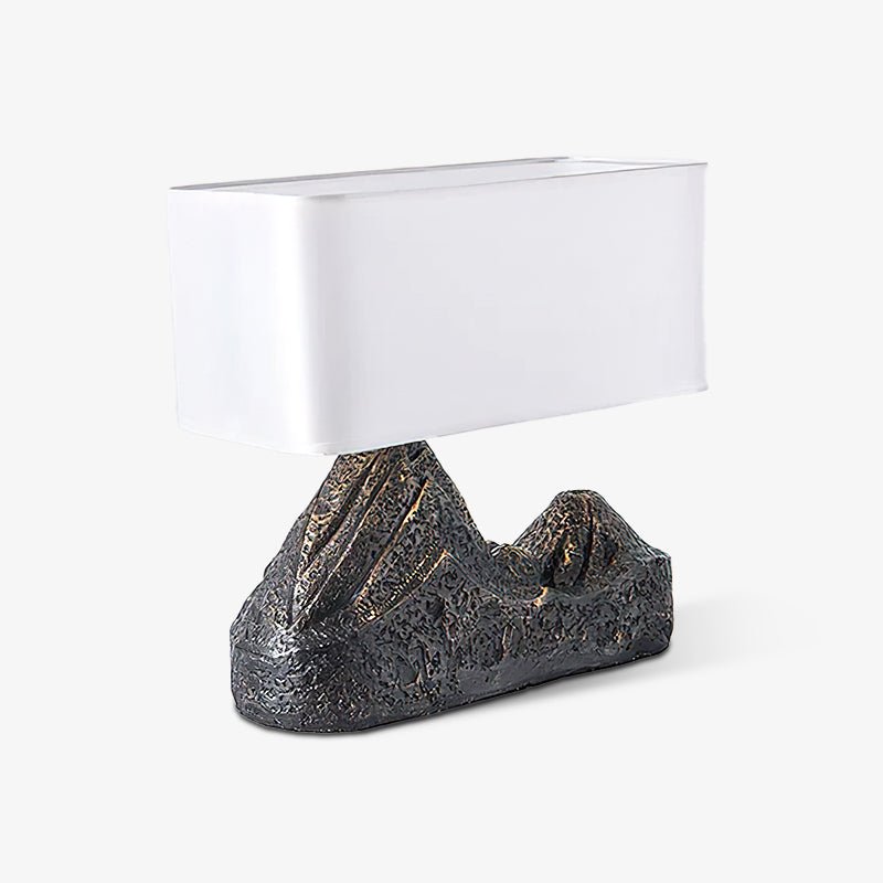 Angled studio view of a Clérachic table lamp with a boxy white shade and a rough bronze-brown mountain base, on light grey.