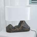 A Clérachic table lamp with a rounded white shade and a bronze-brown mountain base, on a white cabinet by a lace curtain.
