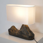 This Clérachic table lamp lit warm on a white cabinet, its glossy white shade above a ridged bronze-brown twin-peak base.