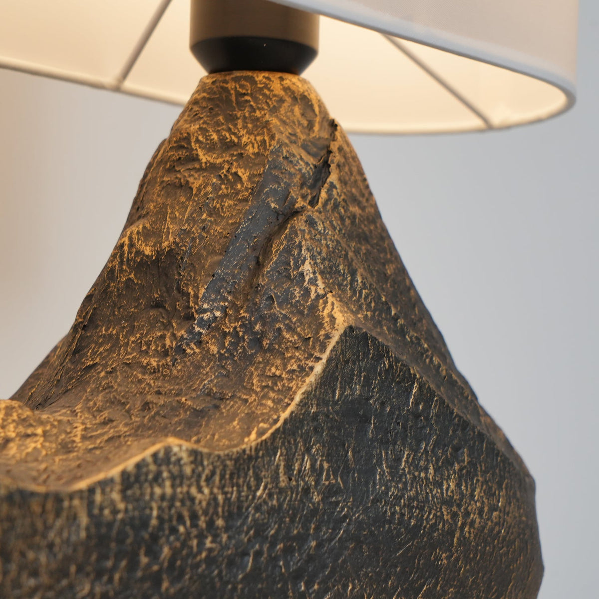 Close view of the carved peak and black fitting where the shade meets the bronze-flecked base of this Clérachic table lamp.