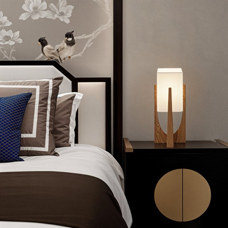 Clérachic table lamp in natural wood on a black bedside cabinet, its rectangular shade lit beside a bed.