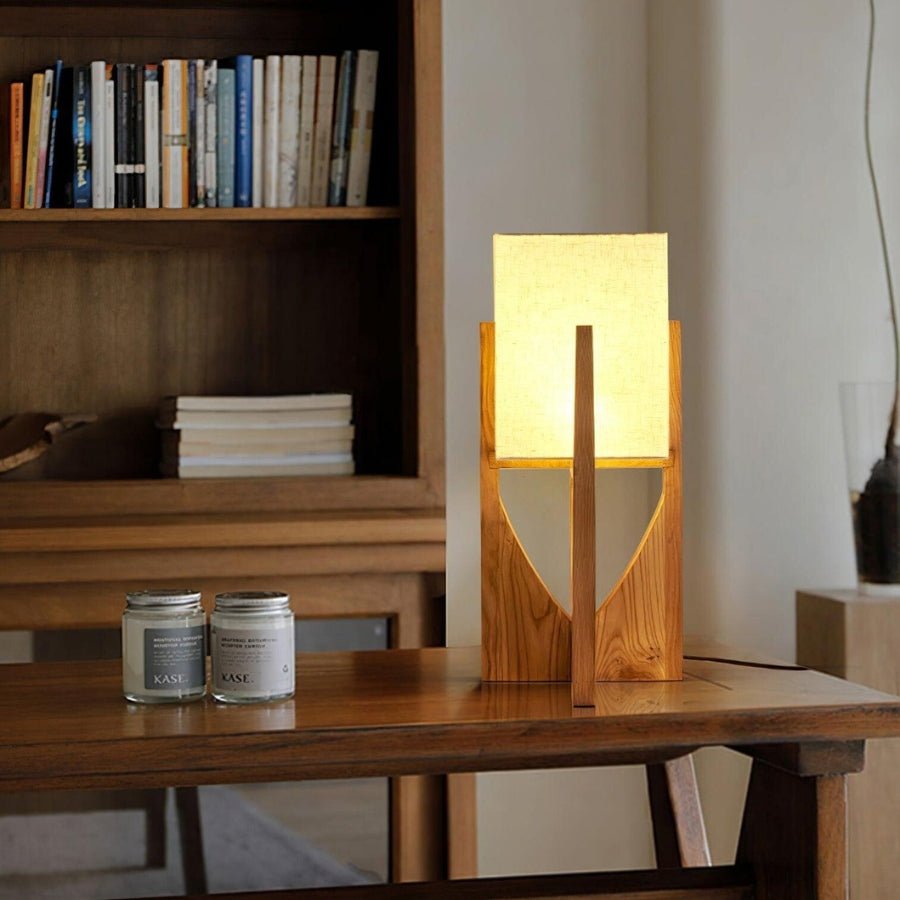 Clérachic table lamp in warm wood glowing on a wooden console, with books on a shelf and two jars beside it.