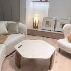 Clérachic wooden table lamp lit on a low shelf beside a cream sofa and a hexagonal coffee table in a living room.